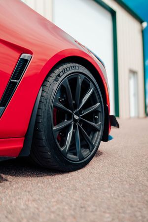 Close-up of a red sports car’s black front wheel and fender on a driveway