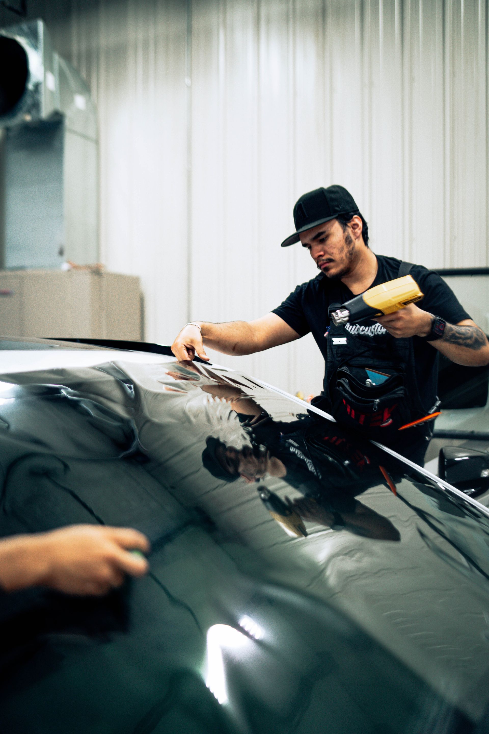 Person squeegeeing a black car windshield in a garage, applying film or polish.
