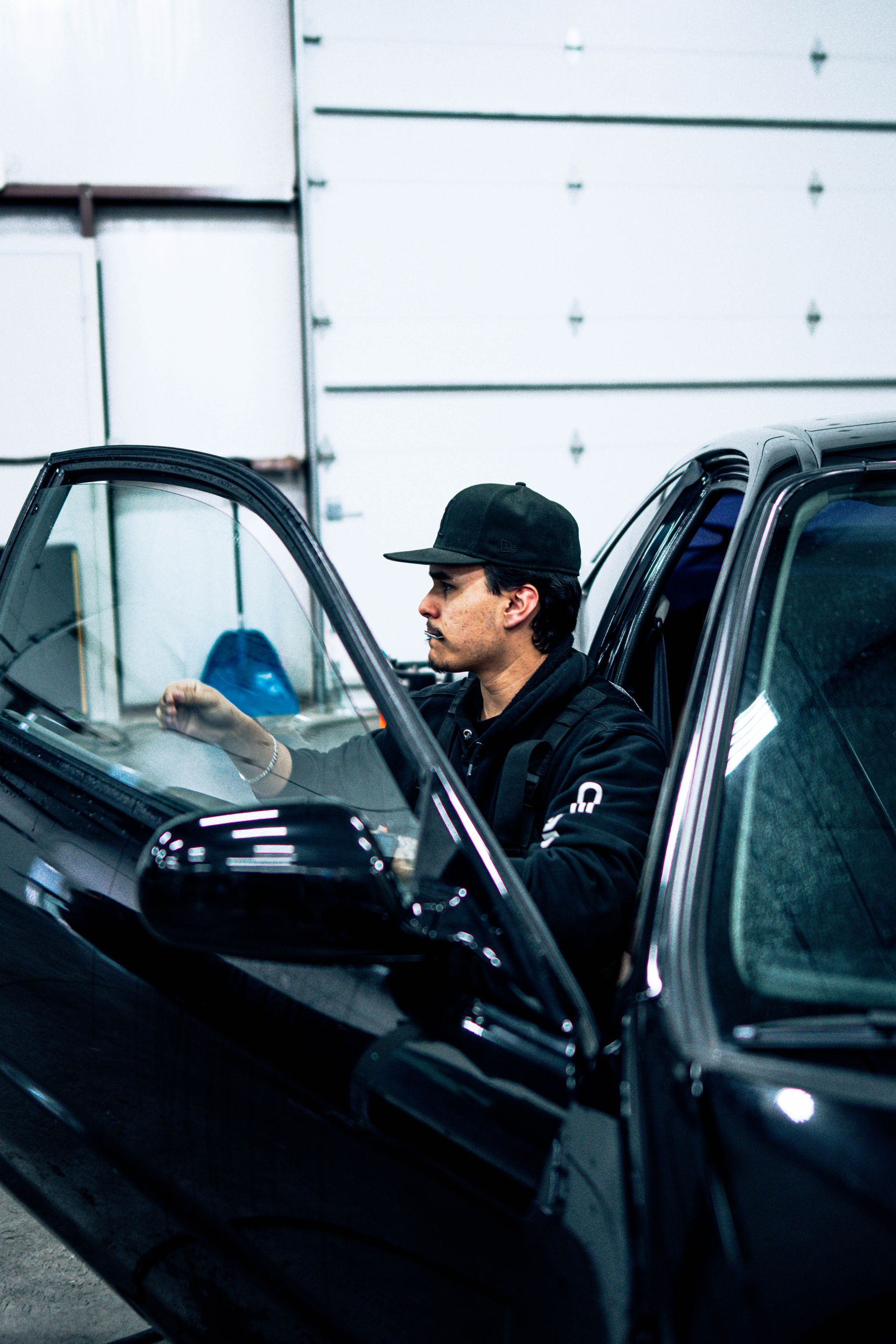 Man in a black cap standing by an open car door in a garage