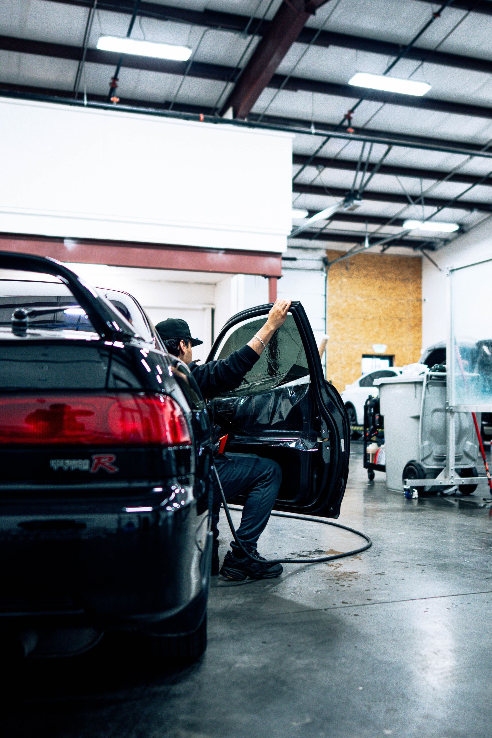 Person cleaning a black car inside an auto repair shop with the trunk open