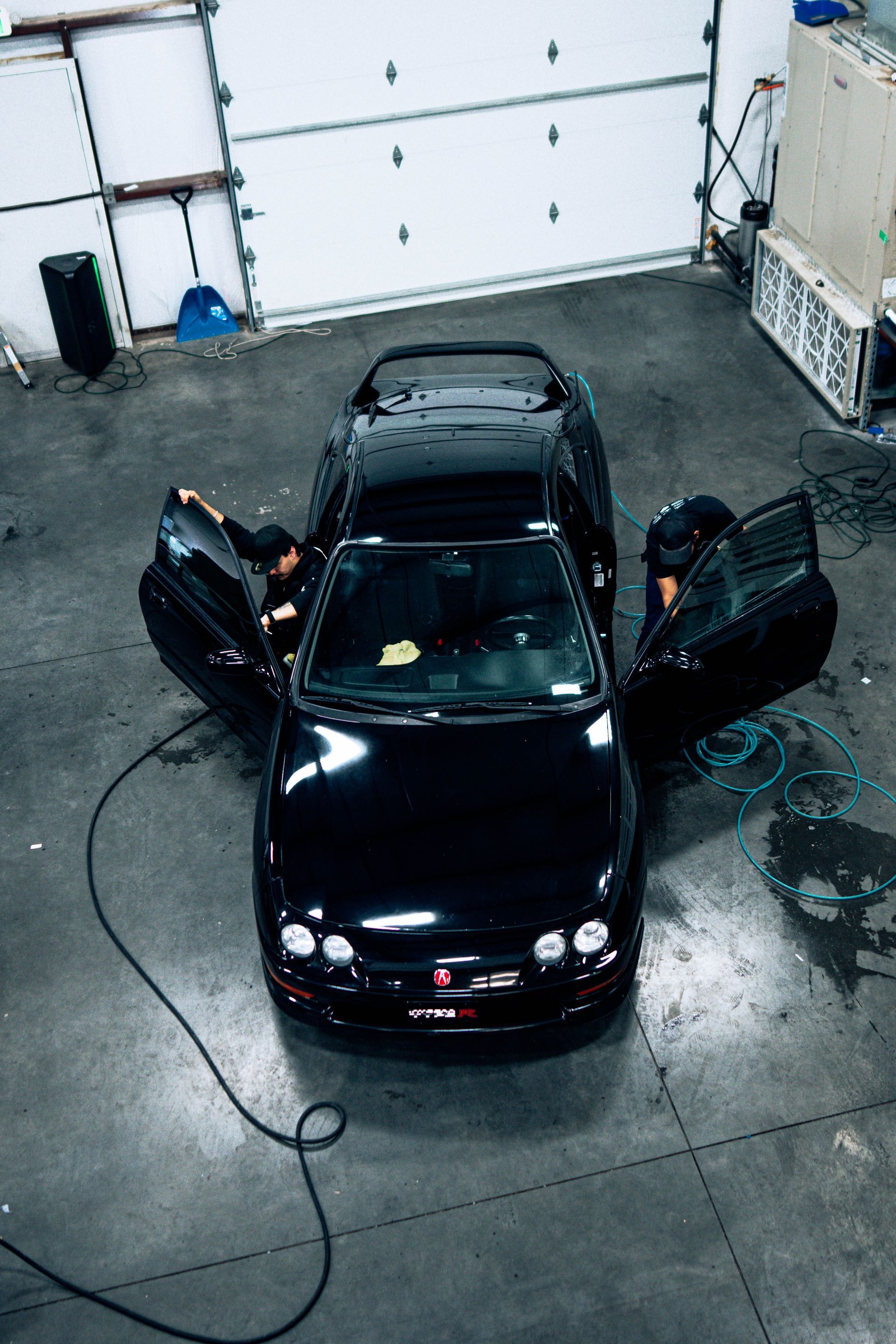 Black car in a garage with both front doors open, seen from above.