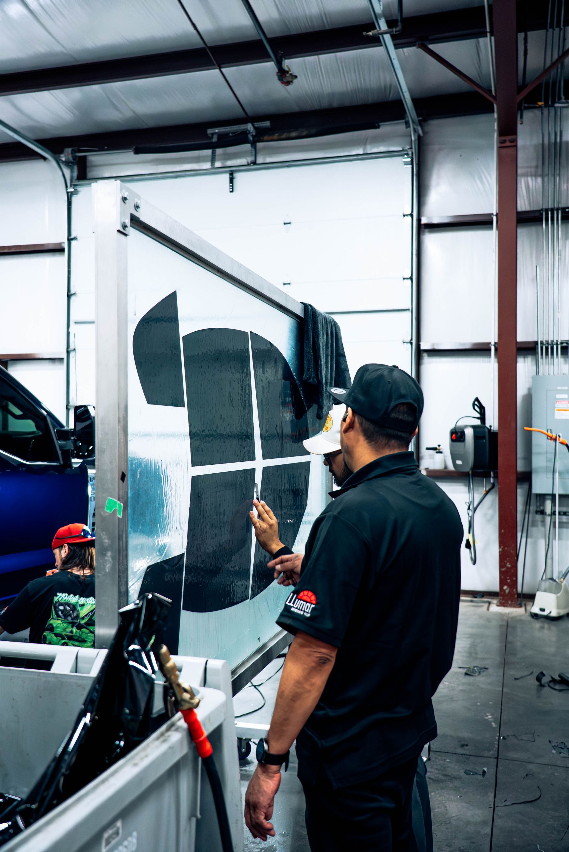 Man painting a wall mural in a workshop garage, using dark gray paint on white panels