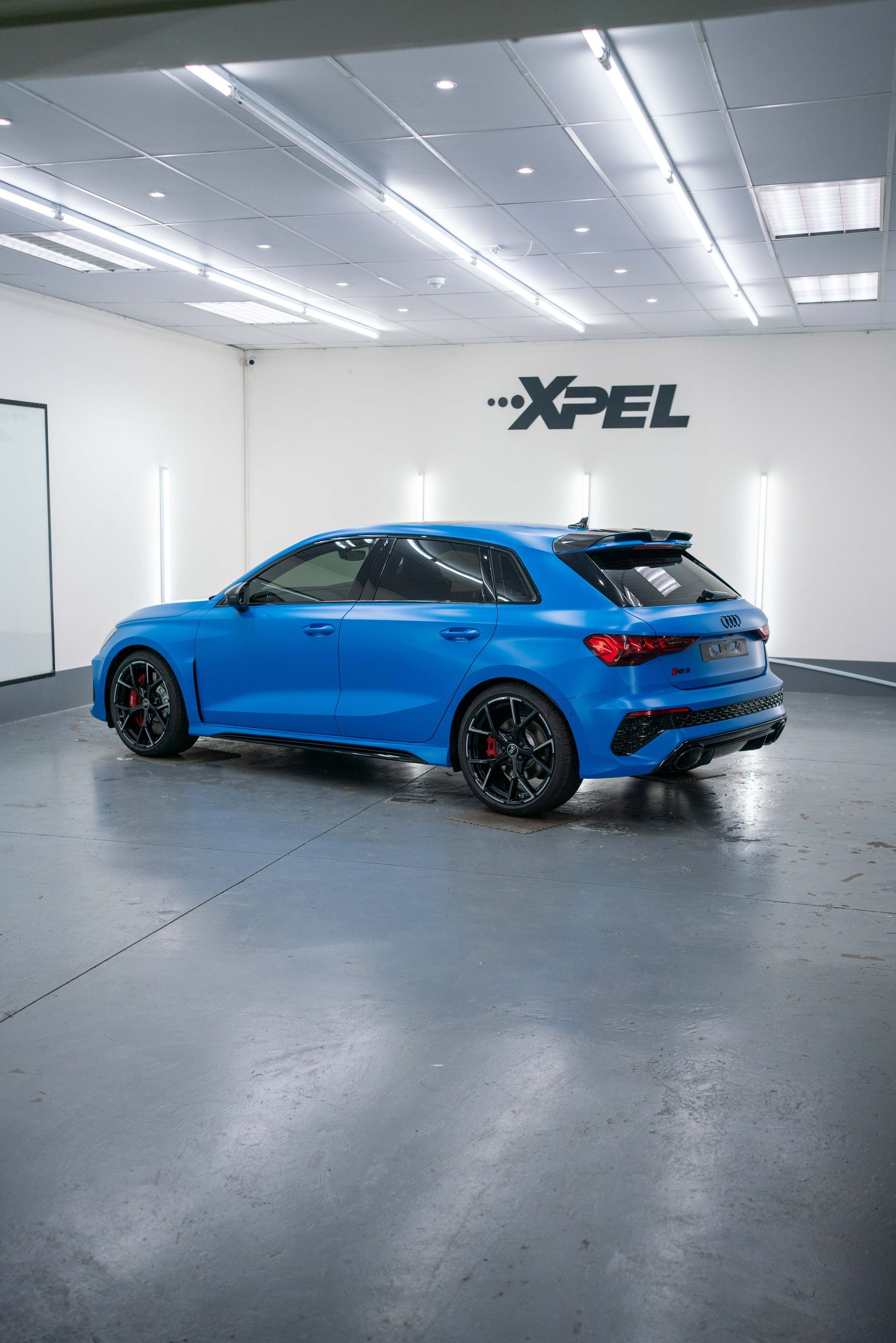 A close-up, high-angle shot of a bright blue Audi RS 3 sportback rear, highlighting its taillight and sporty black trim.