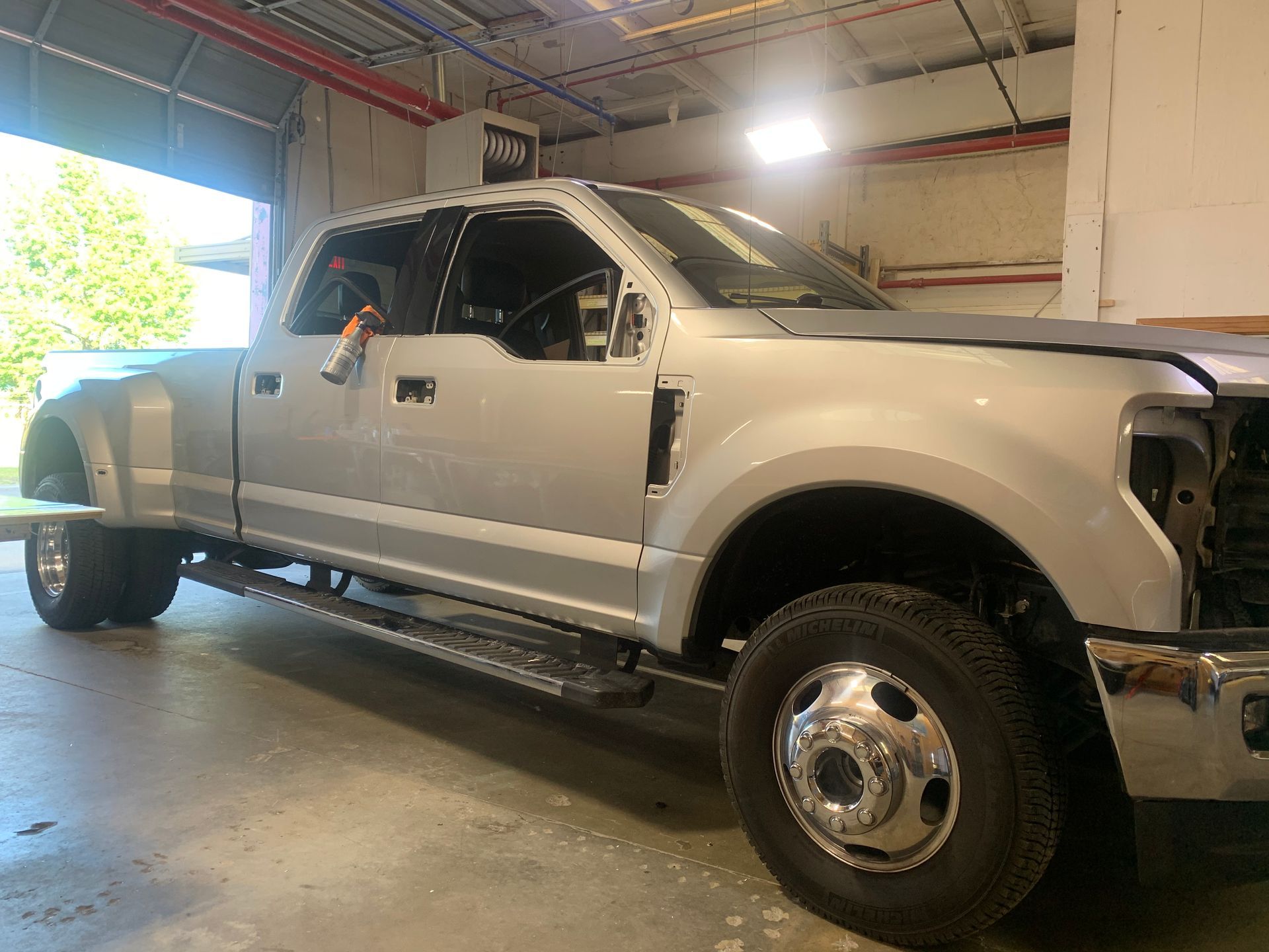 A silver Ford dually truck undergoing repairs in a brightly lit automotive workshop.