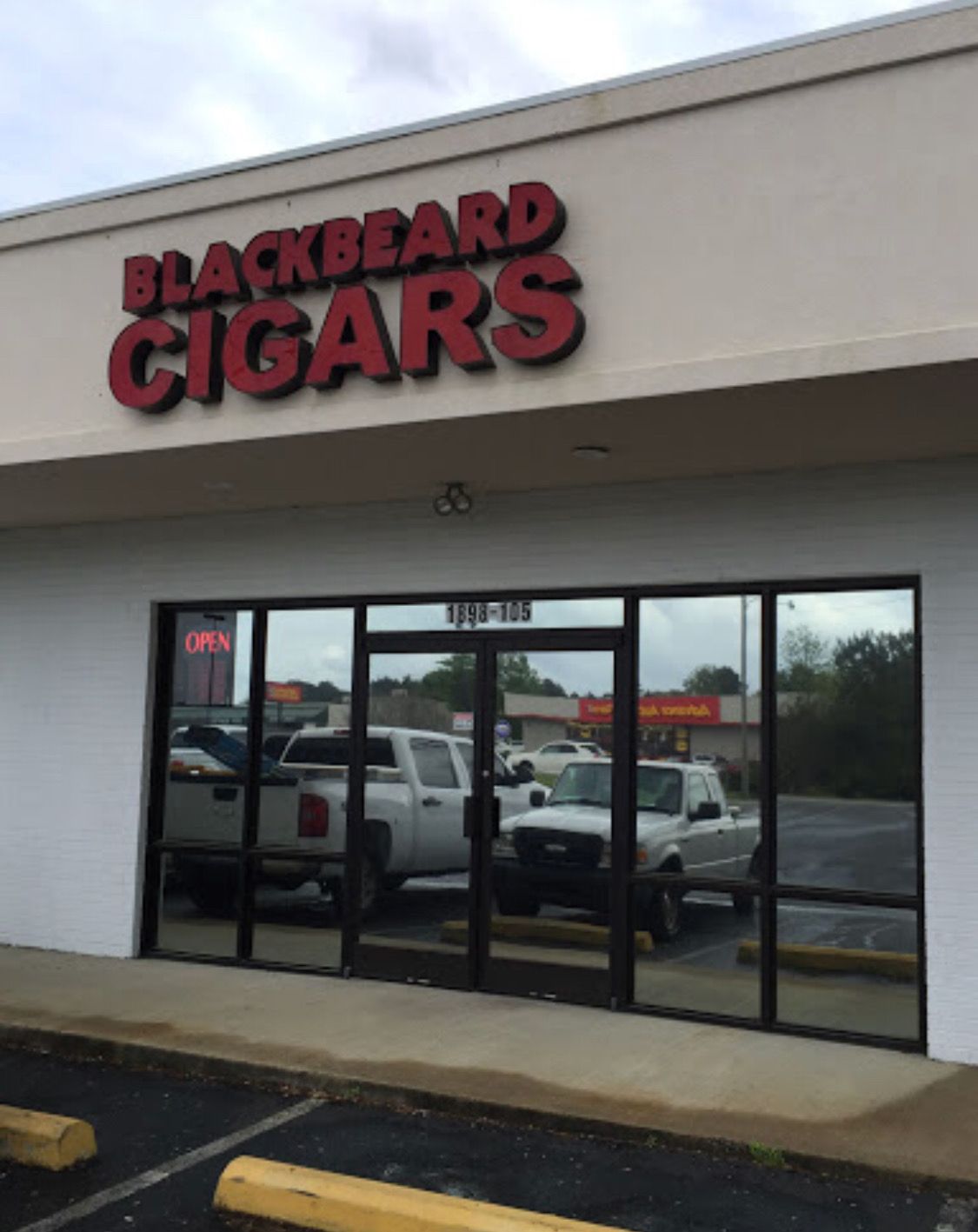 Storefront of Blackbeard Cigars with dark red lettering on a beige wall above glass doors and windows.
