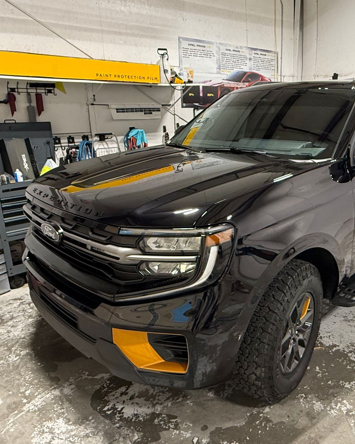 A black Ford Expedition with yellow bumper accents parked inside a brightly lit automotive garage.