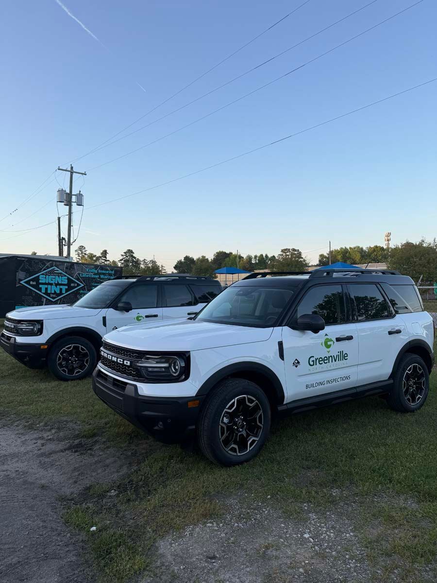 Two white Ford SUVs parked on grass at dusk, with company logos on the doors.