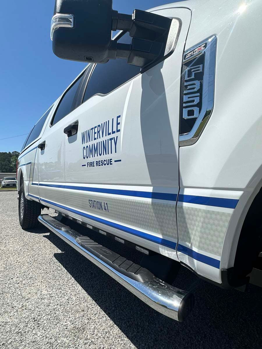 Side view of a white Trinity Community pickup truck with blue stripes and chrome steps