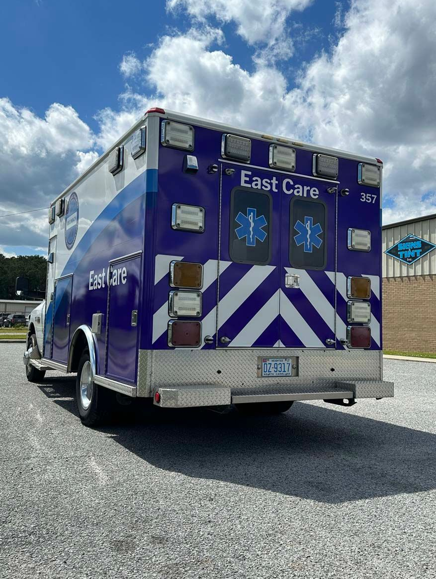 Blue East Care ambulance rear view with white chevron stripes parked outdoors under a cloudy sky