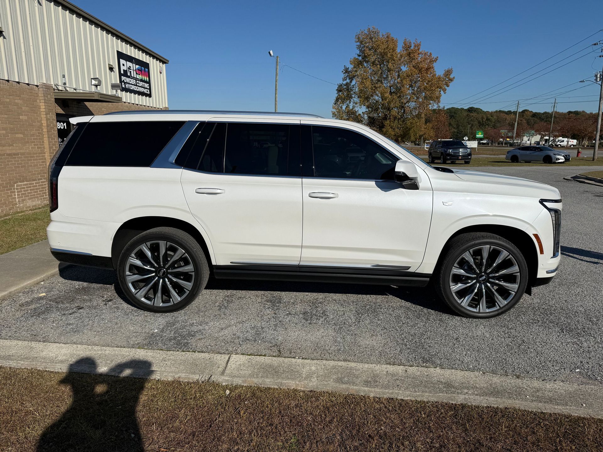 A white Cadillac Escalade parked on a gravel lot outside a building on a clear day.
