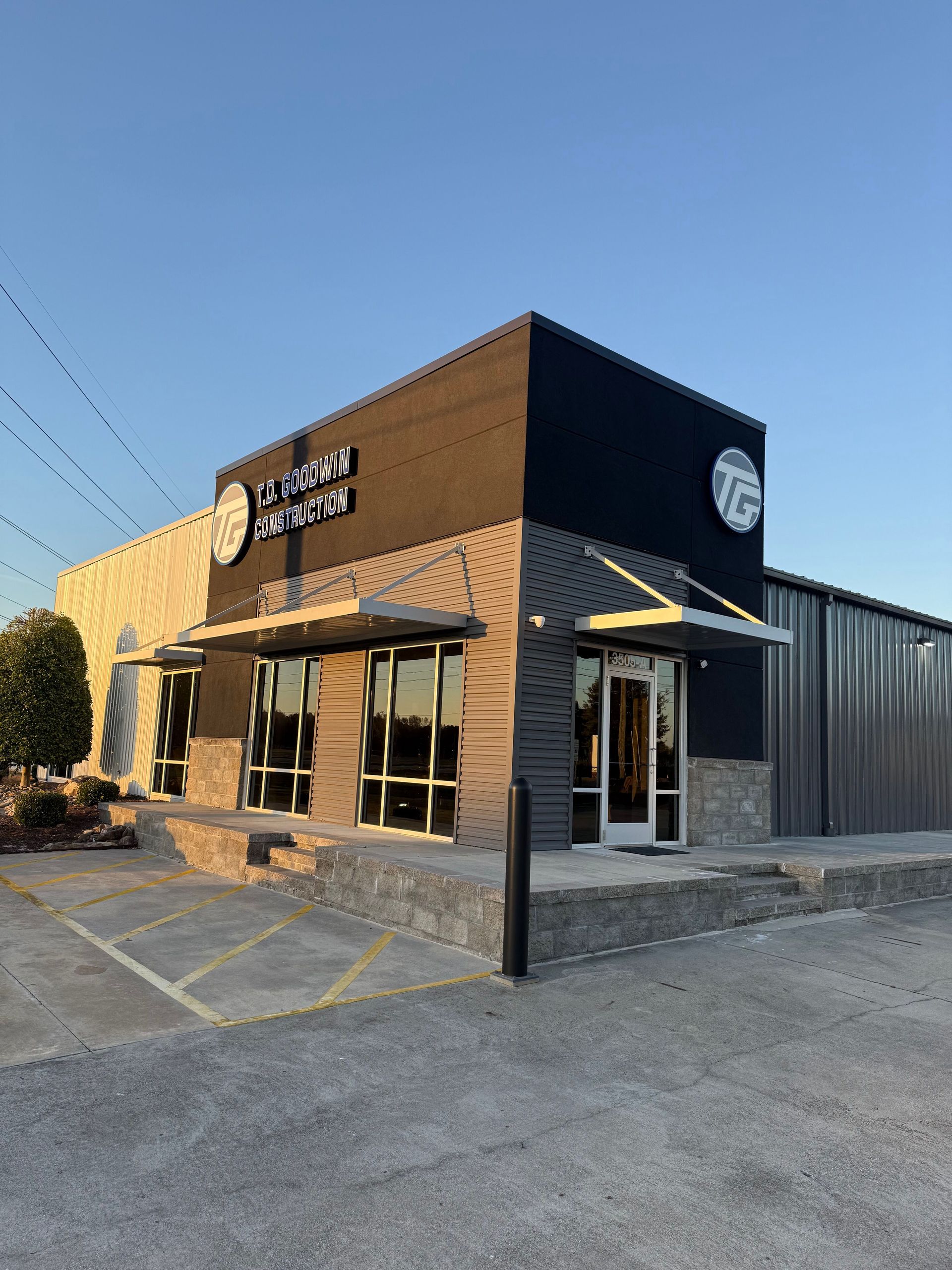 A modern commercial building exterior with black and stone accents, large glass windows, and a corner entry under an awning.