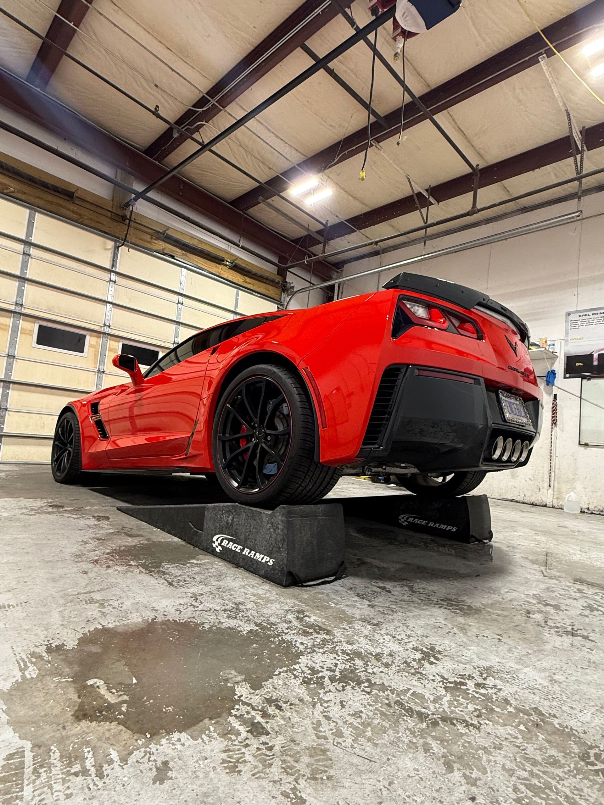 A bright red sports car parked on black vehicle ramps inside a garage with a large overhead door.