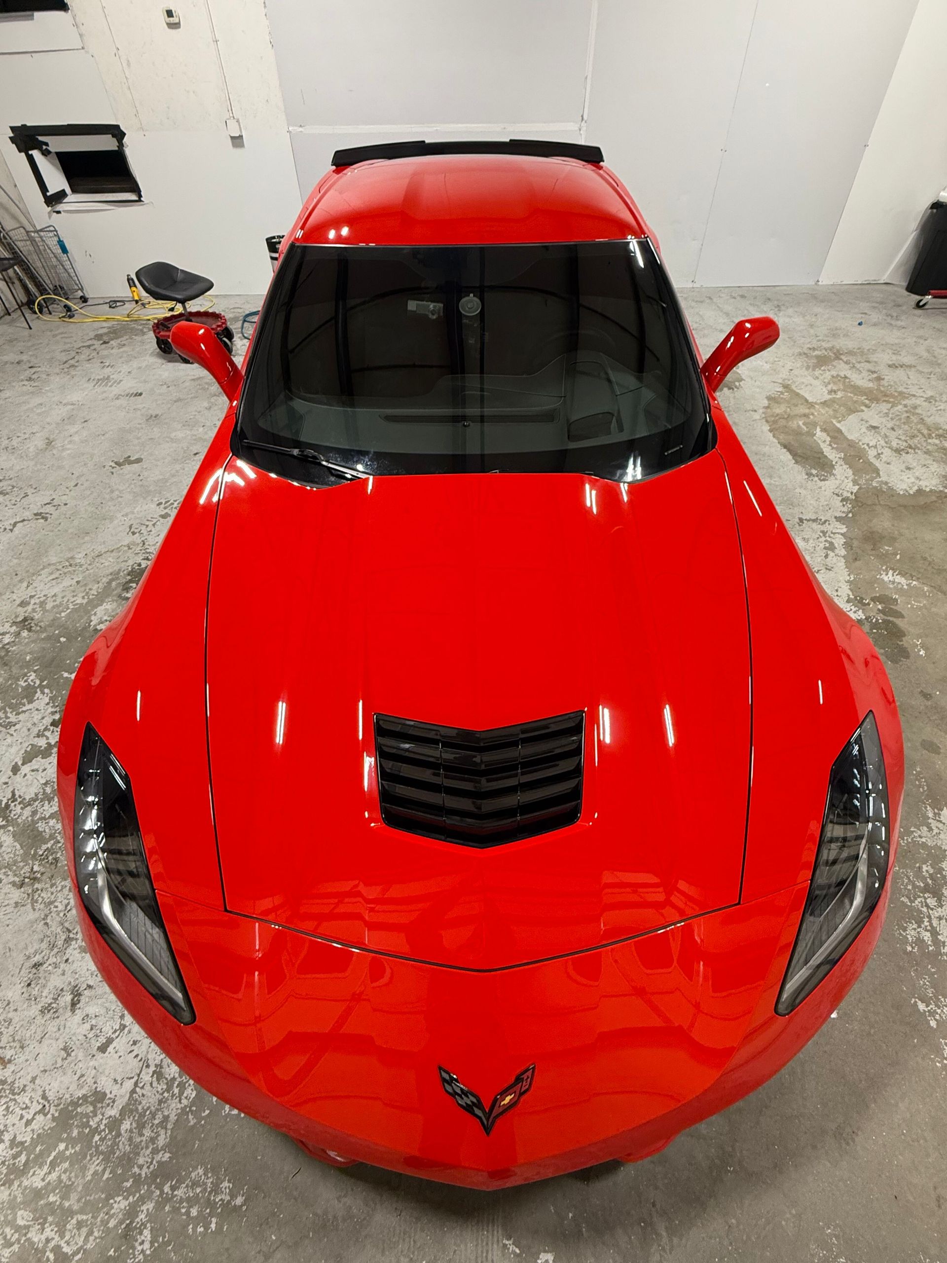 High-angle view of a bright red Chevrolet Corvette parked in a garage with a concrete floor.