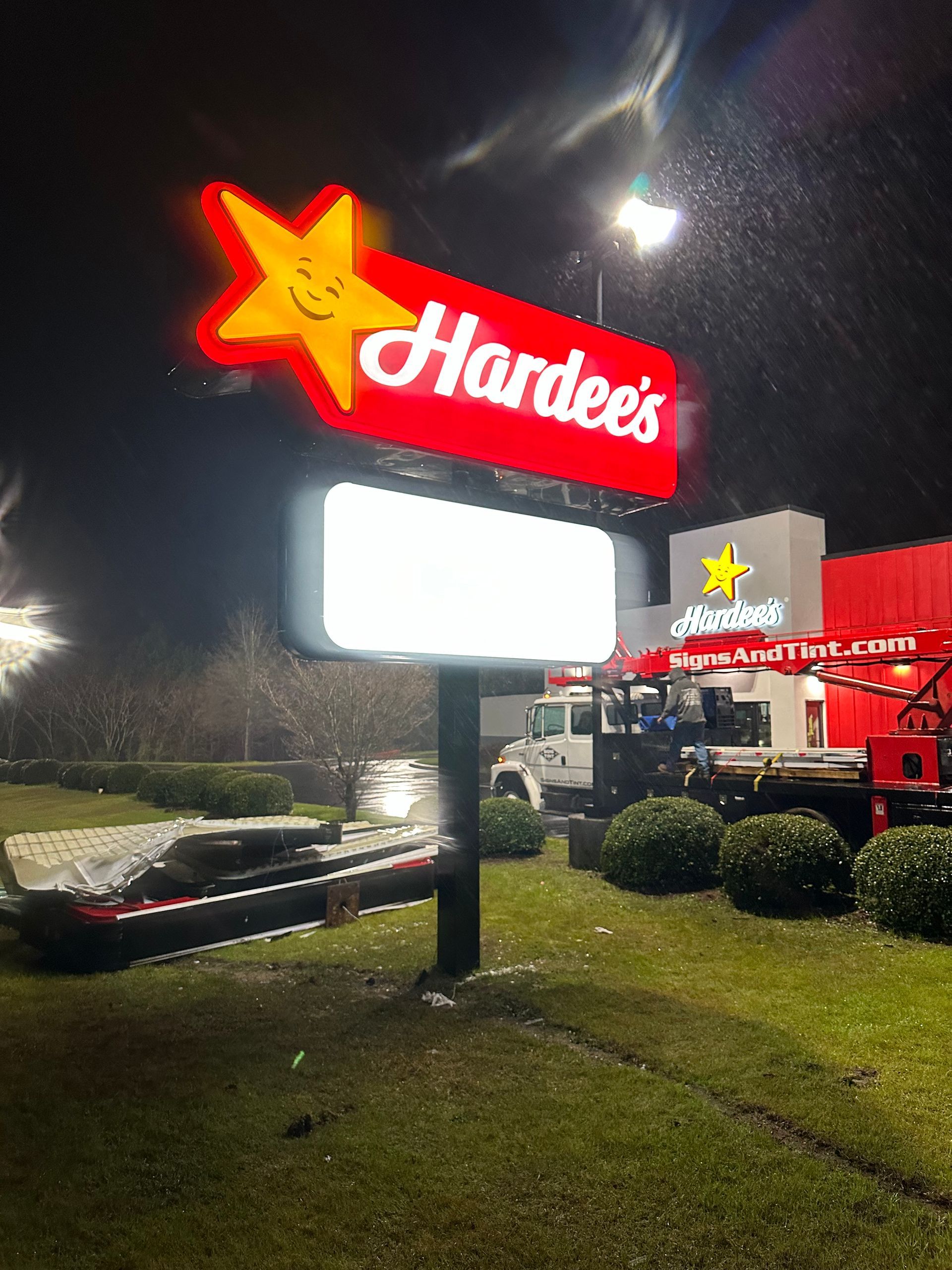 Illuminated Hardee's restaurant sign at night with a service truck parked near the building.