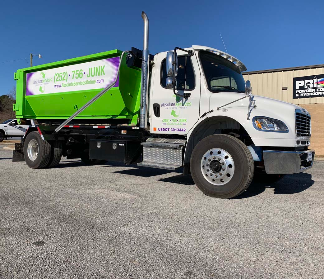 Green-and-white dump truck parked on gravel under a clear blue sky