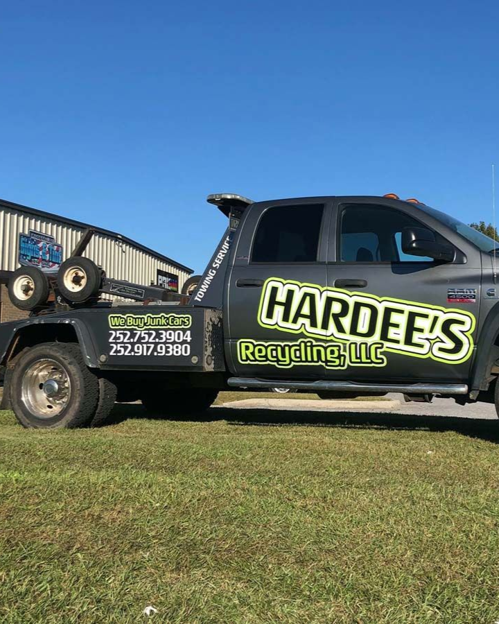 Black pickup tow truck with Hardee's Recycling LLC logo parked on grass under a blue sky