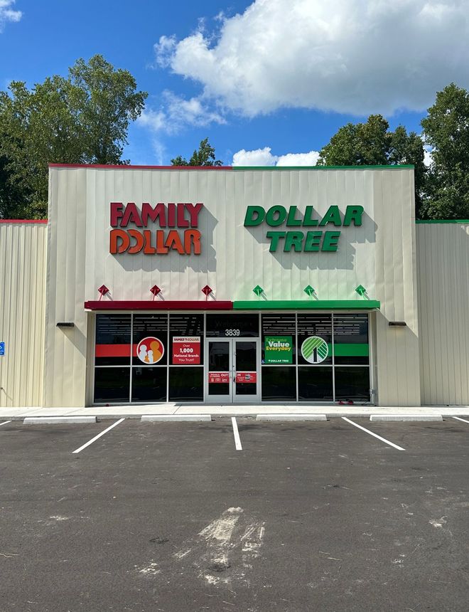 A dual-branded Family Dollar and Dollar Tree store under a clear blue sky, featuring a large parking lot in the foreground.