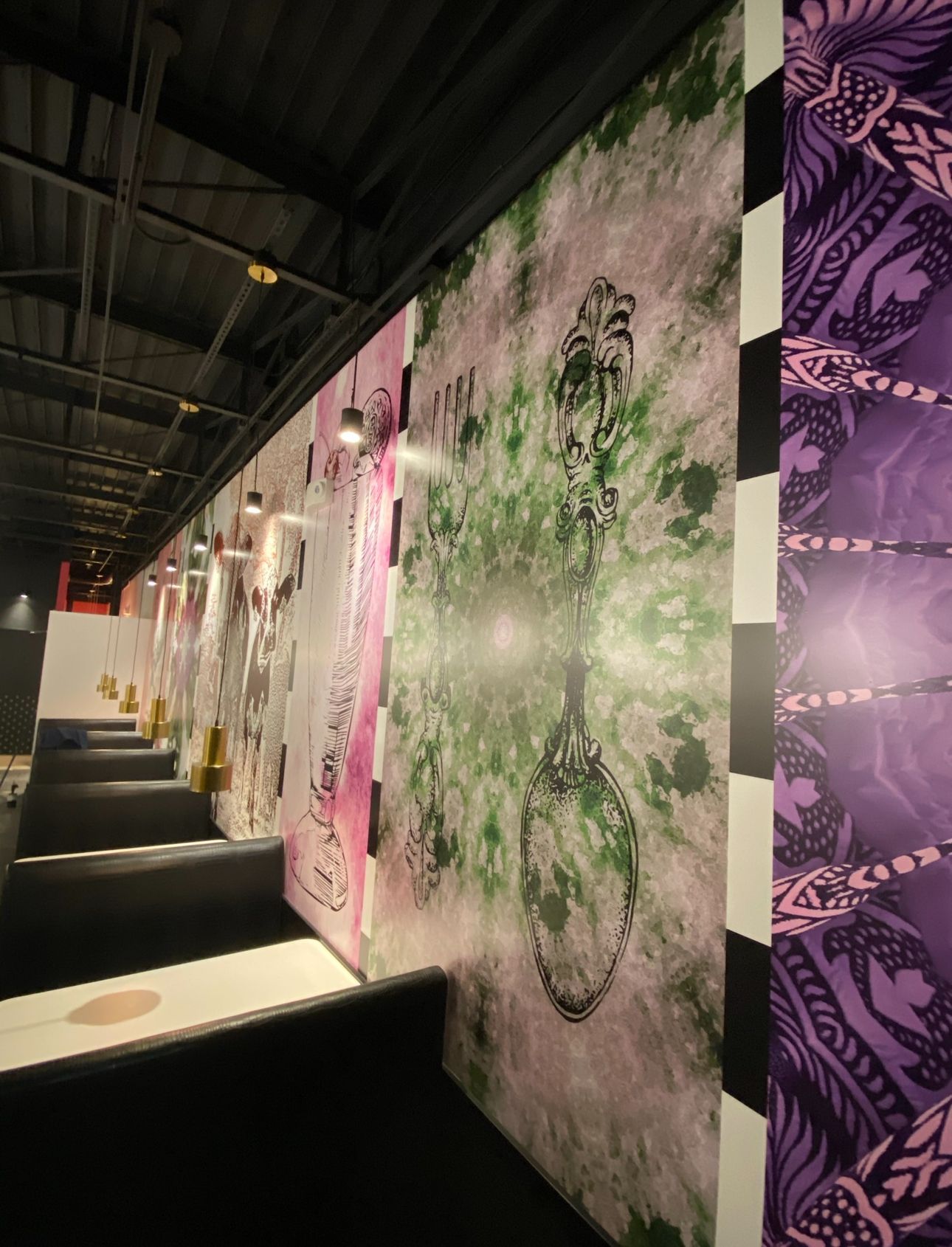 A row of sleek booths lines a wall decorated with large, vertical abstract art panels in green, pink, and purple.