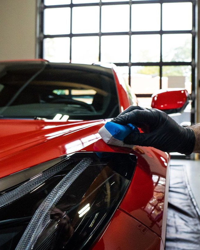 A bright orange Ferrari parked inside a dimly lit professional automotive garage with high-contrast ceiling lighting.