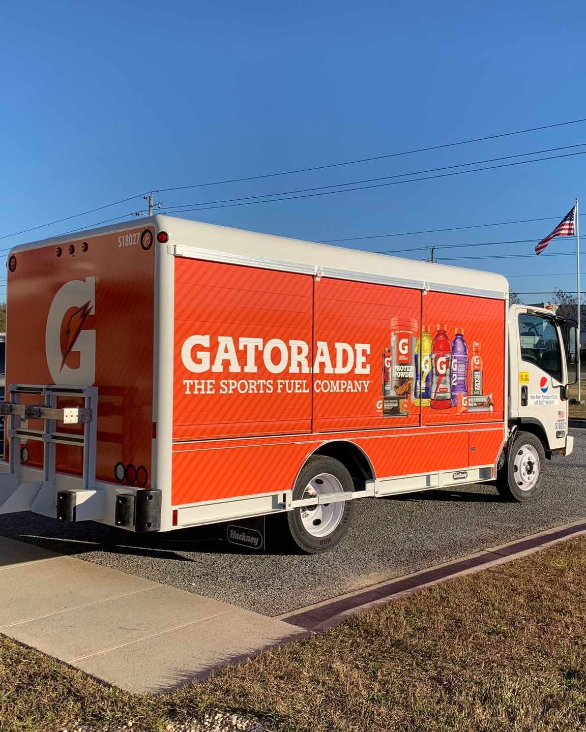 A bright orange Gatorade delivery truck parked outdoors on a gravel lot under a clear blue sky.