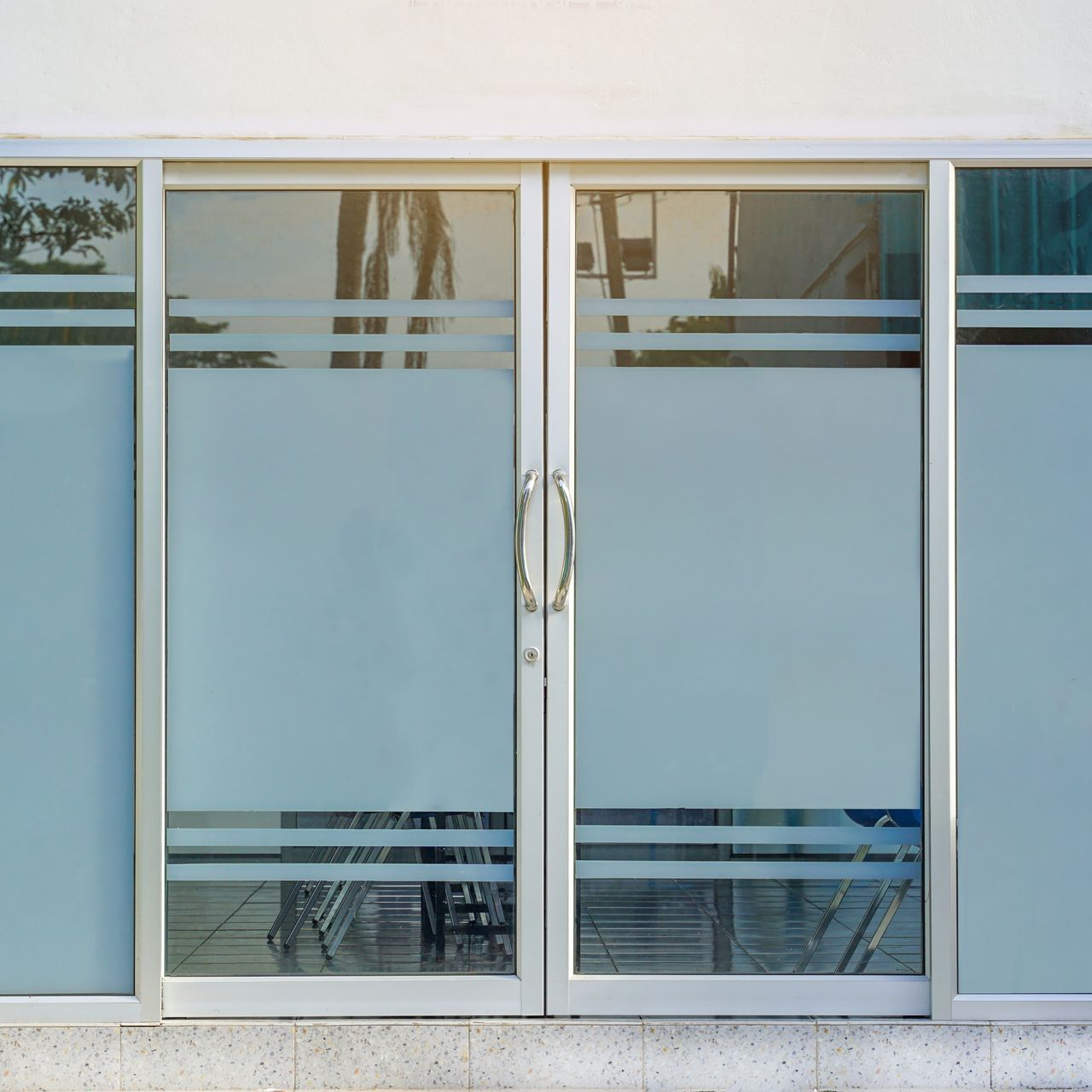 Double glass doors with silver frames and frosted privacy film featuring horizontal clear stripes.