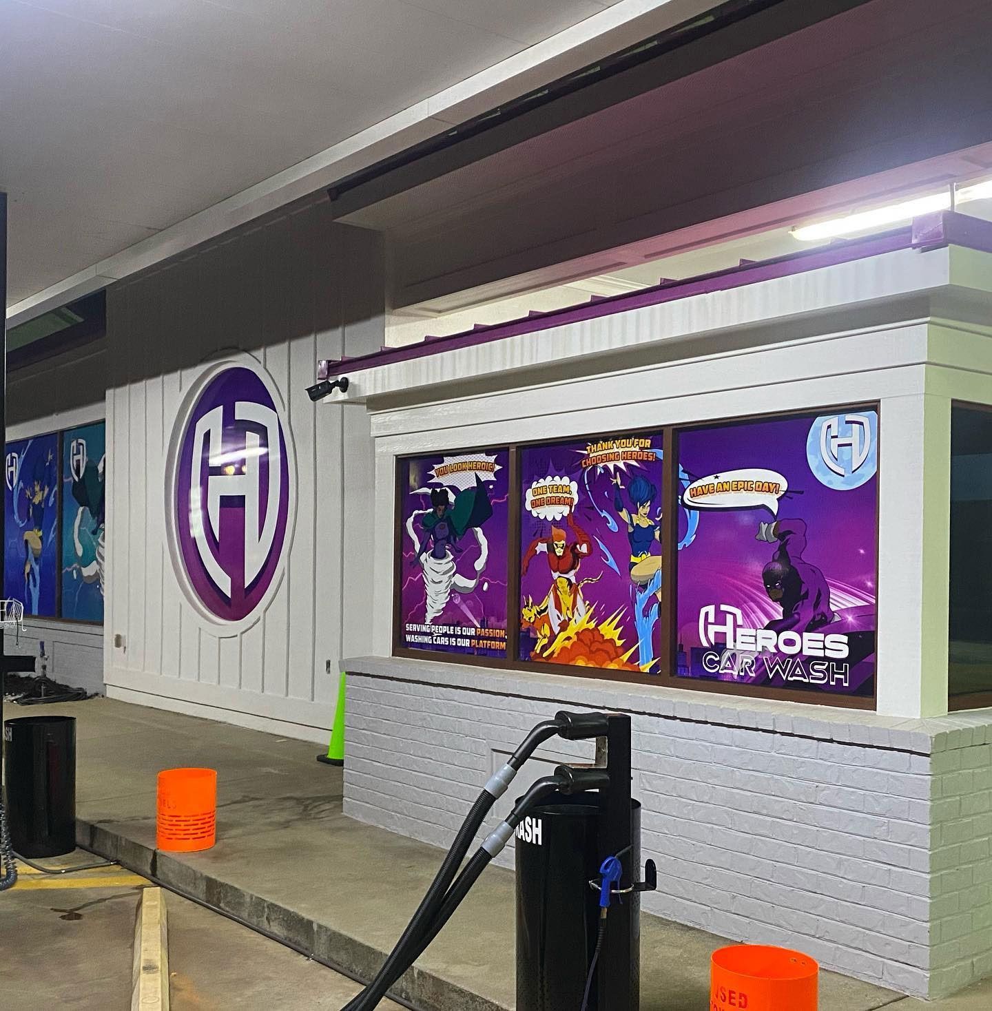 Purple storefront windows with superhero graphics beside a gas pump at a convenience store