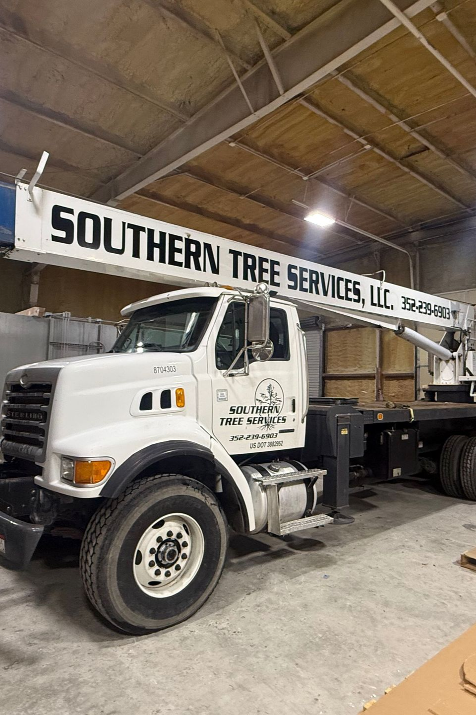A white Southern Tree Services, LLC crane truck parked inside a warehouse.