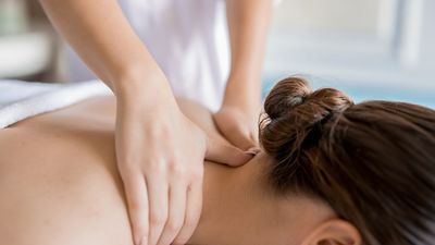 Hands giving a shoulder massage to a person lying face down on a white spa bed