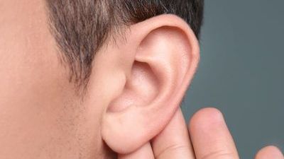 Close-up of a person’s ear with a finger touching behind it