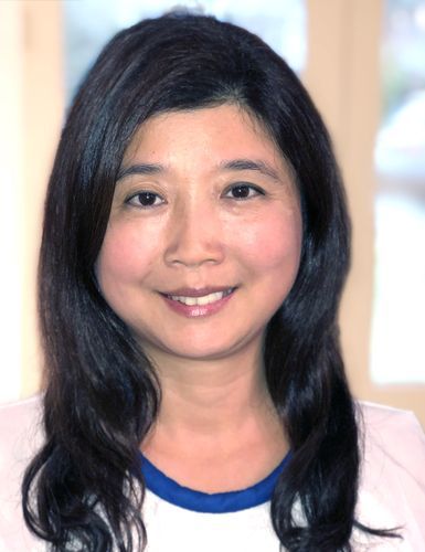 Portrait of a smiling person with long dark hair, wearing a white top with a blue collar