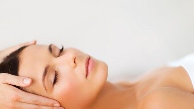 Woman lying on a white bed receiving a facial massage with eyes closed