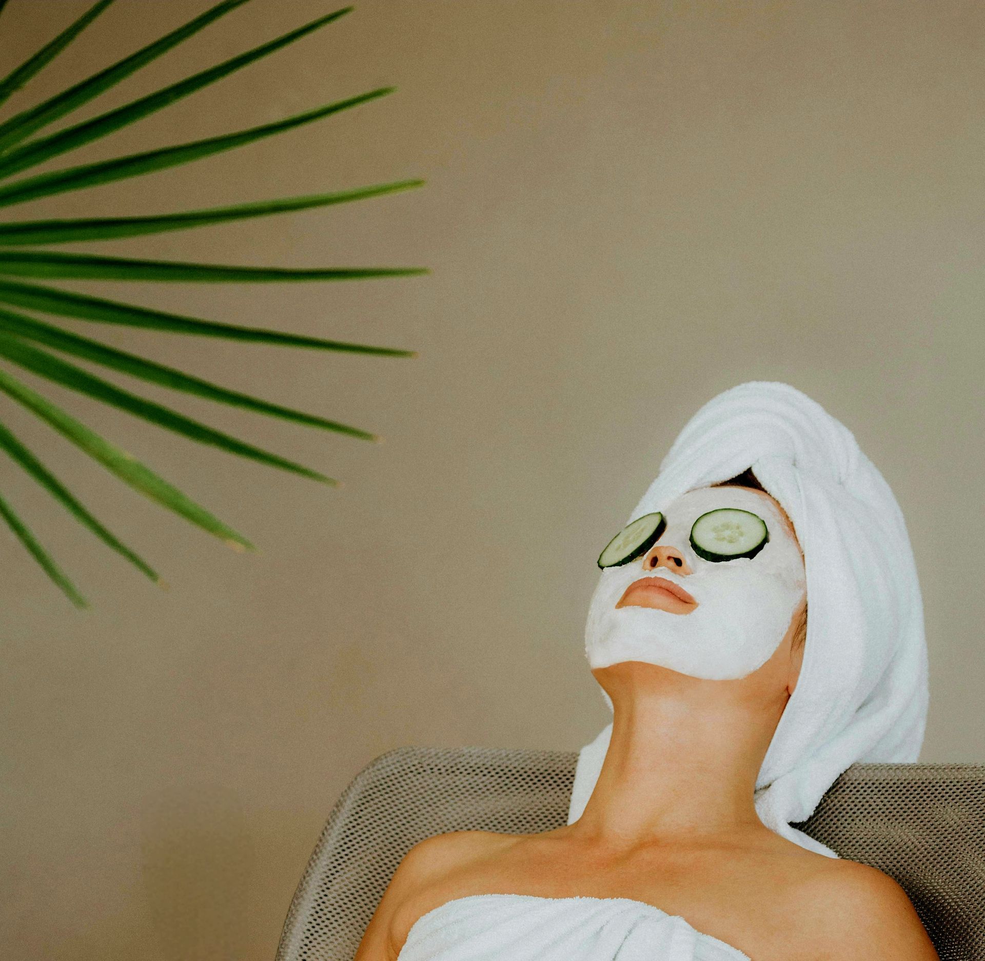 Woman reclining with a towel on her head and a face mask, wearing cucumber slices in a spa setting