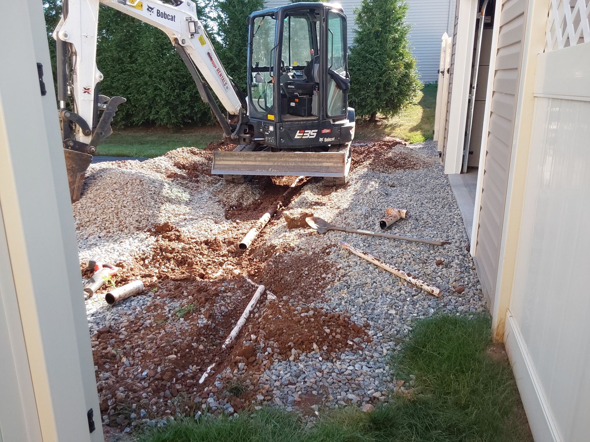 a small excavator is digging a hole in the ground in front of a garage