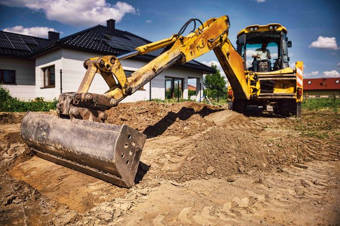 a yellow excavator is digging a hole in the dirt in front of a house