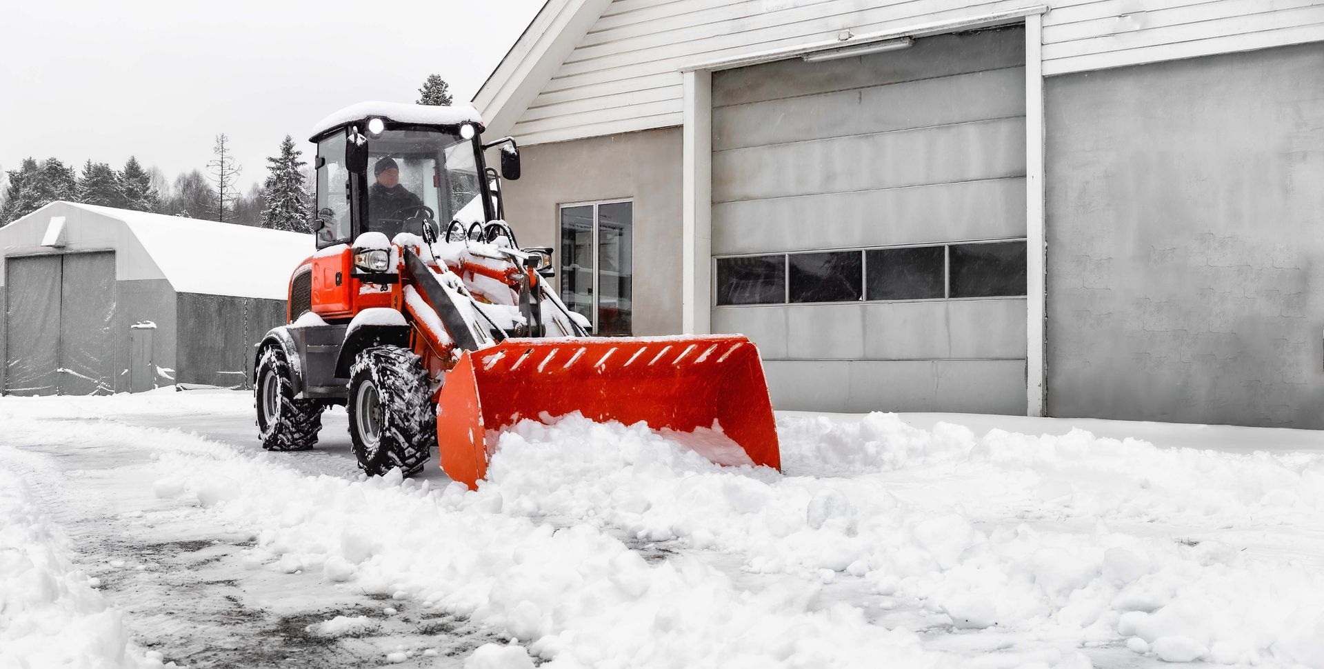 a tractor is plowing snow in front of a garage