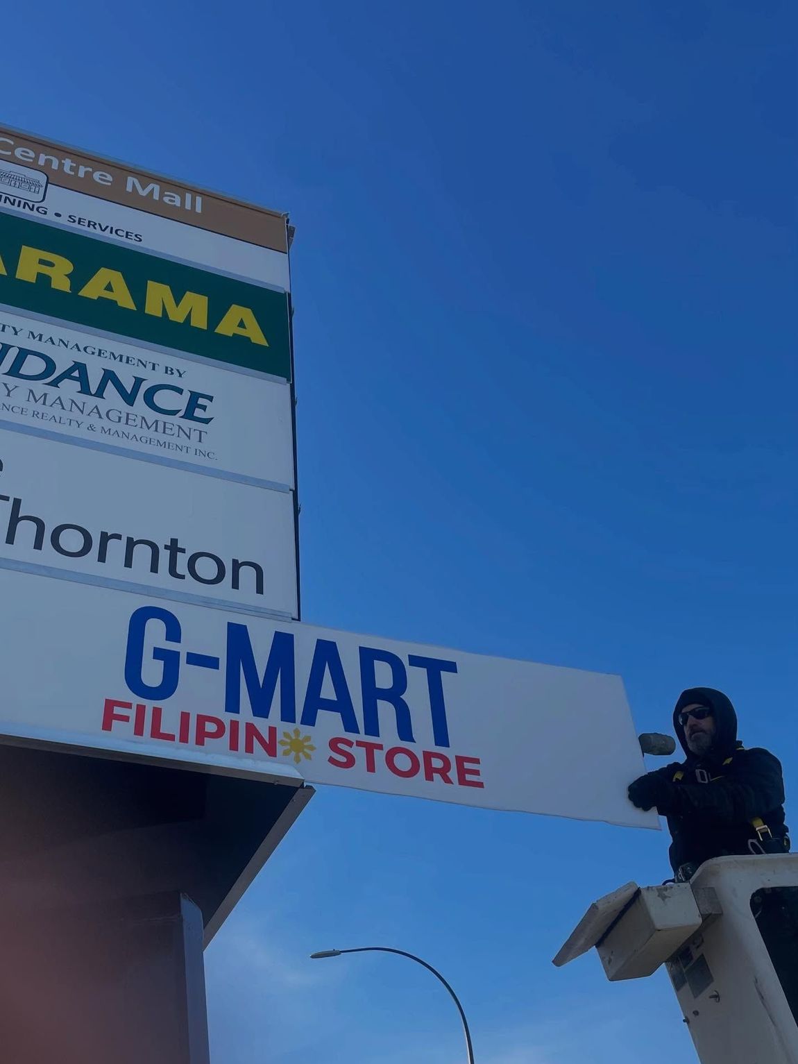 Workers installing a large sign panel on a commercial storefront with bucket truck
