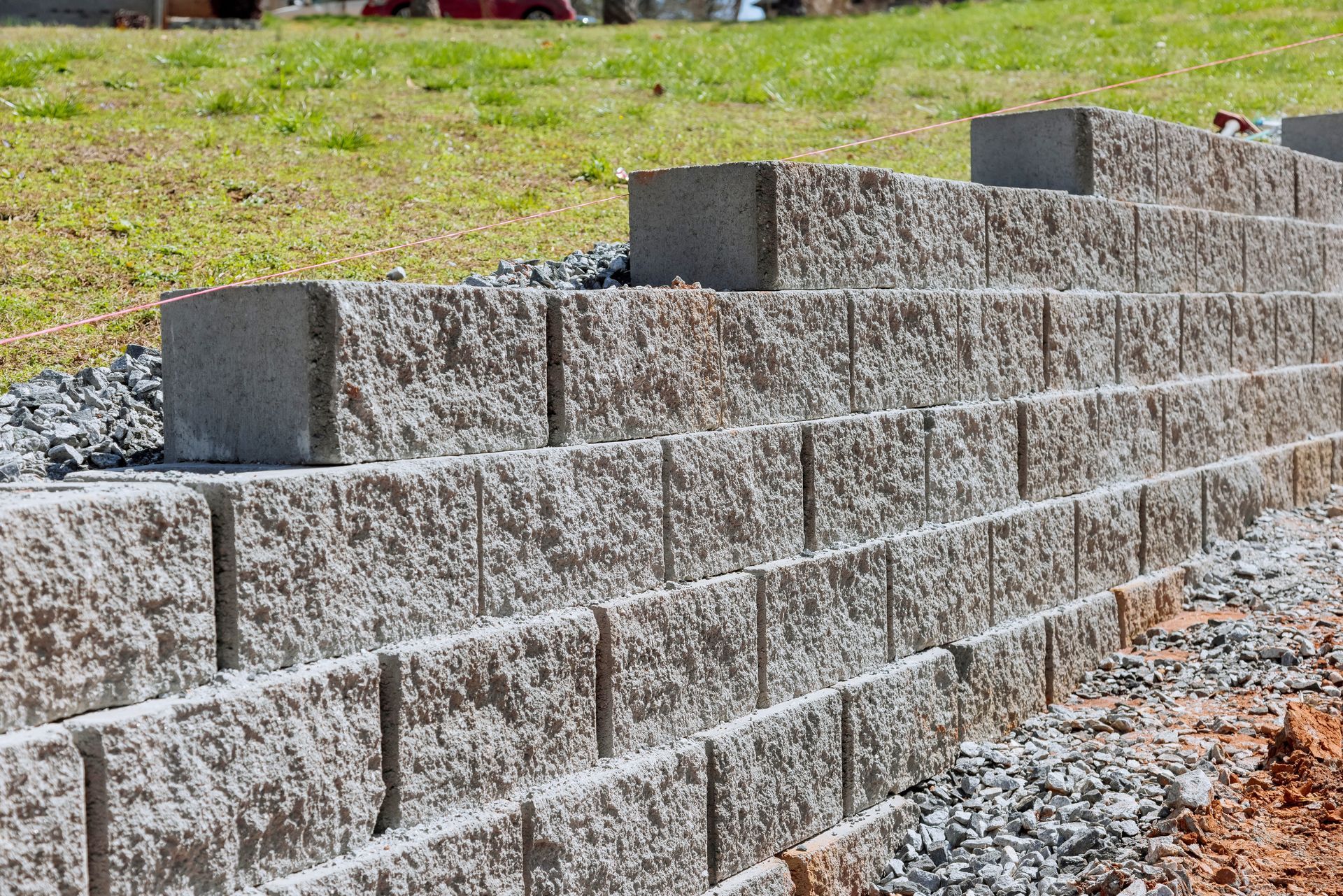 Gray stone retaining wall under construction on a gravel slope beside grass.
