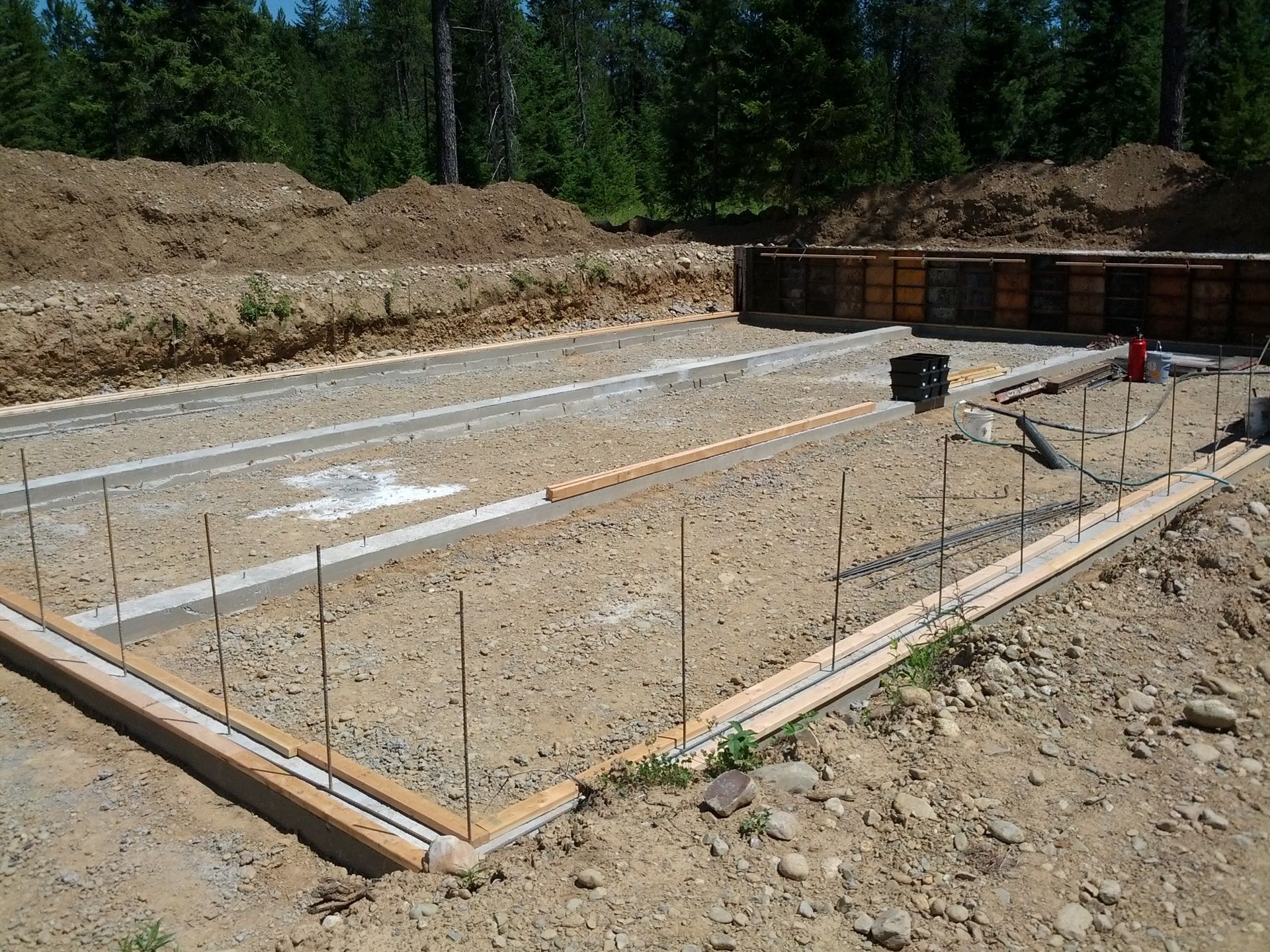 Concrete foundation formwork at a construction site with rebar and gravel ground.