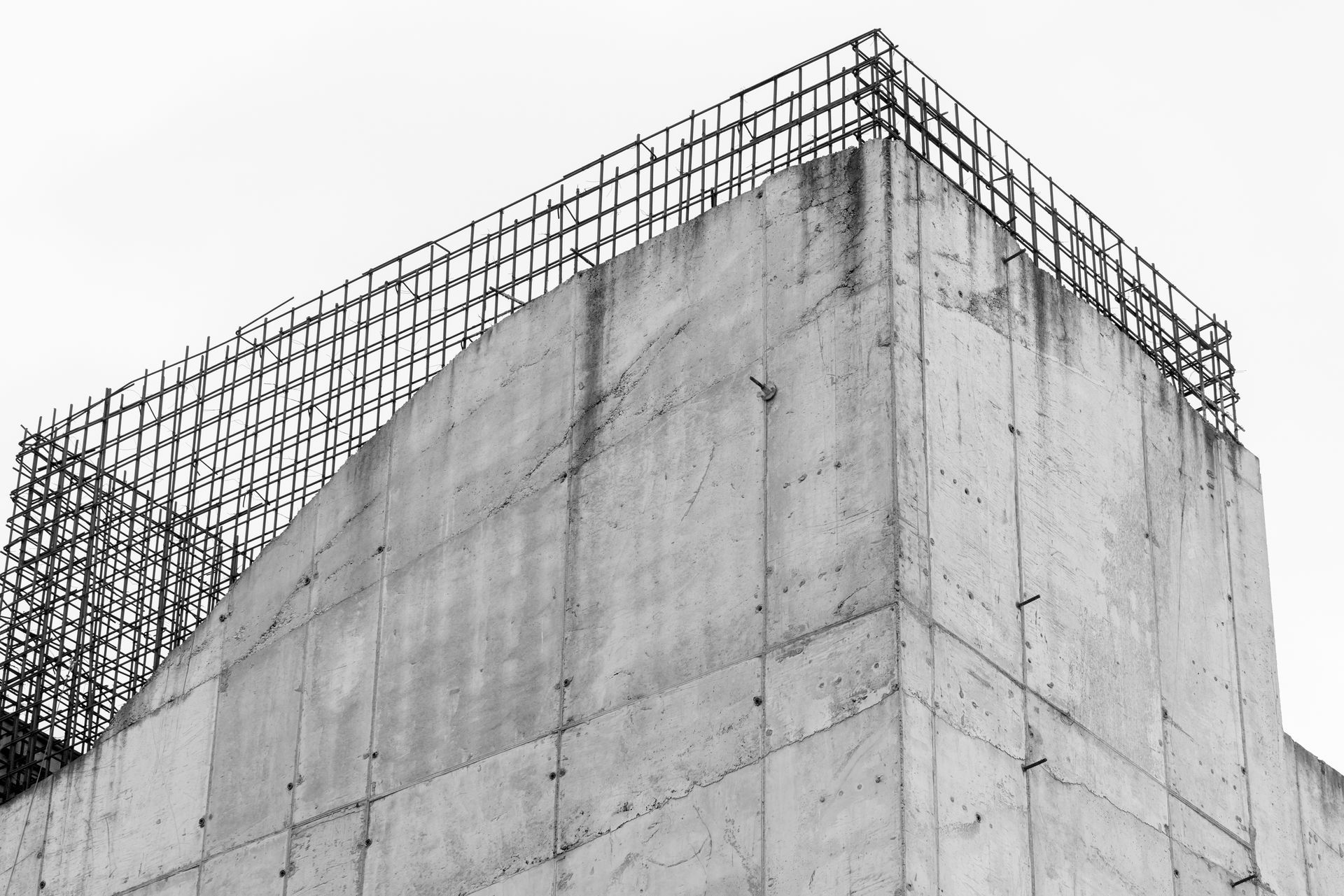 Concrete building corner with exposed rebar against a cloudy sky