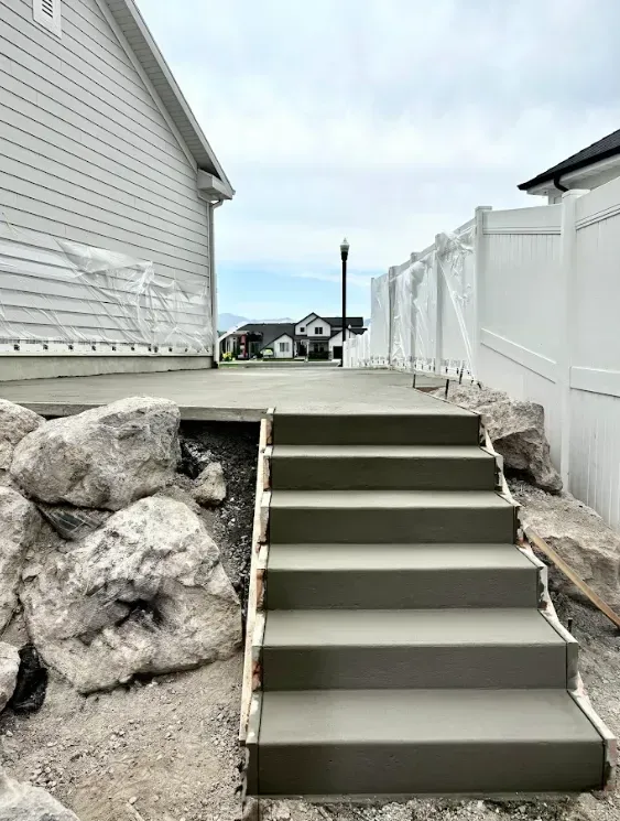Concrete outdoor stairs beside a house, with white fencing and large rocks on both sides.