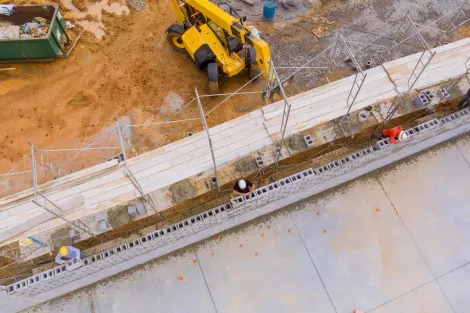 Aerial view of a construction site with a yellow loader beside a long concrete wall and sidewalk.