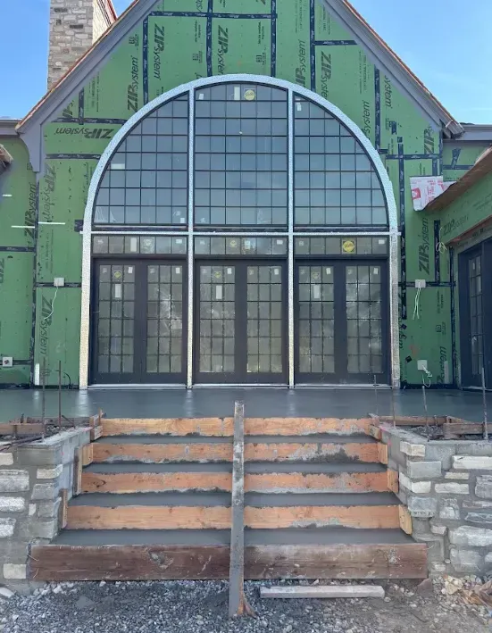 Green house entrance with tall arched windows, front steps, and stone railings