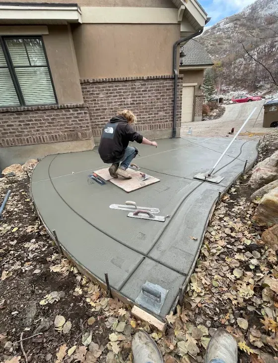 Person smoothing a curved concrete walkway beside a house during construction