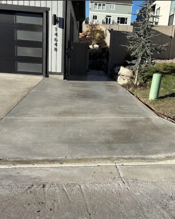 Concrete driveway leading to a gated side yard beside a modern garage, with a green utility box nearby.