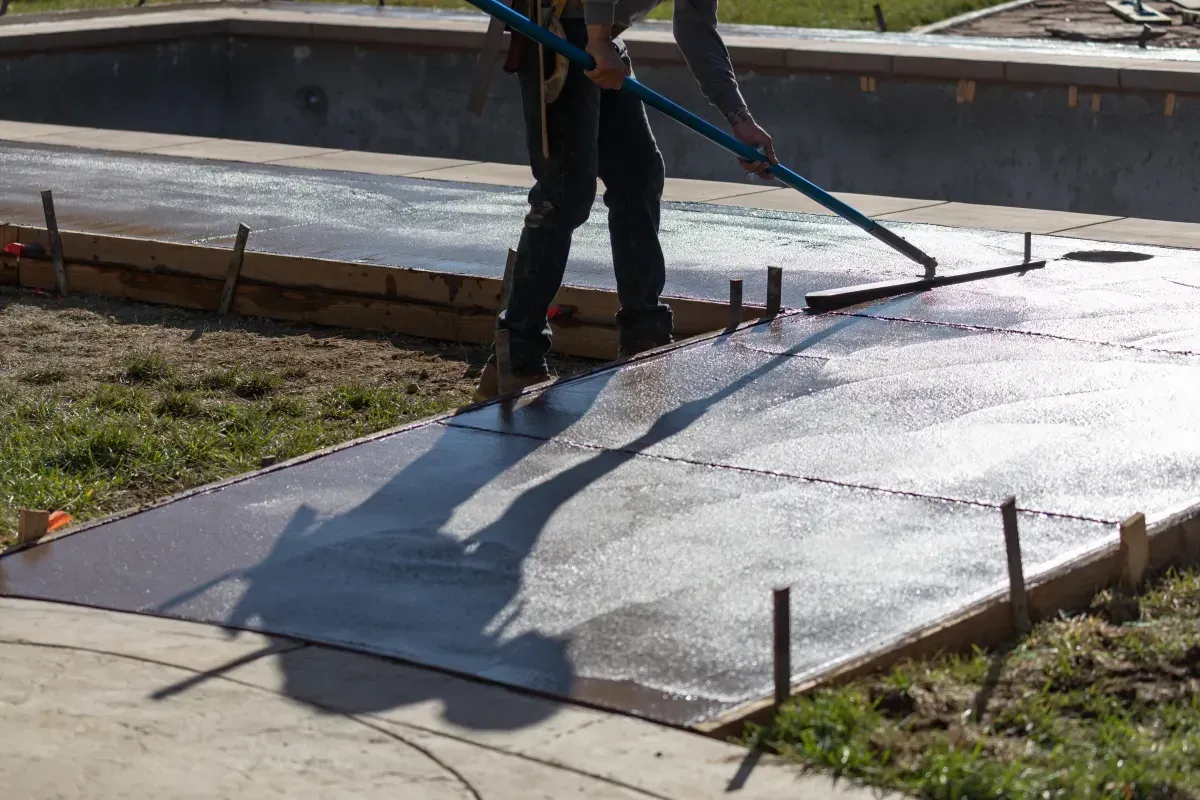 Person smoothing a curved concrete walkway beside a house during construction