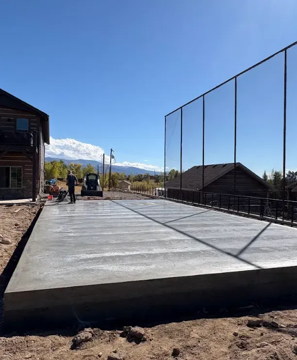 Outdoor sports court under construction with concrete slab, net posts, and mountains in the background