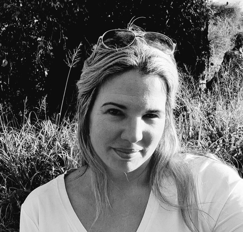 A black-and-white selfie of a person wearing sunglasses on their head, posing in front of tall outdoor grass.