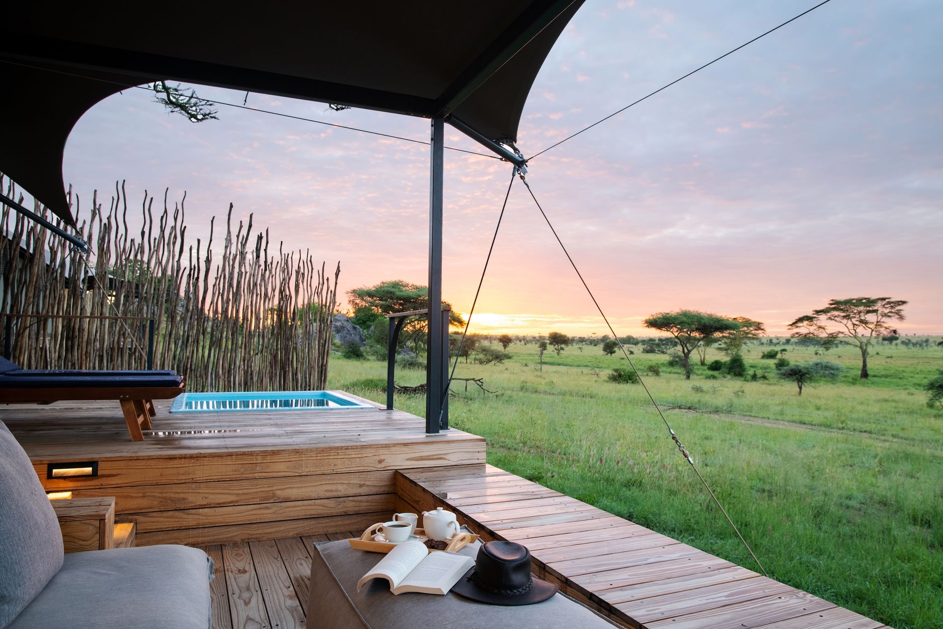 A safari tent deck with a small pool, lounge seating, and a sunset view over the savanna.