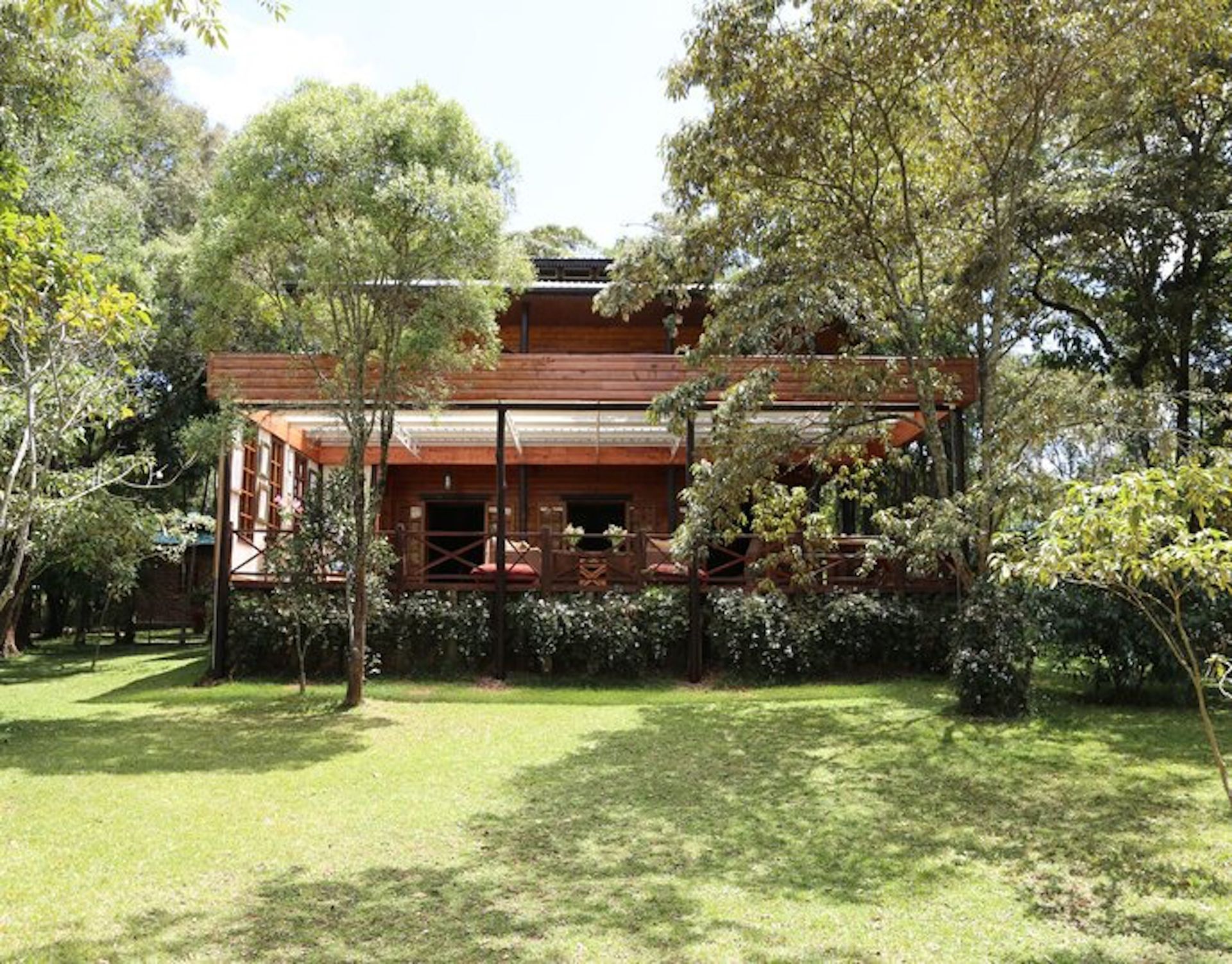 A wooden two-story house with a covered porch set among green trees and a grassy lawn.