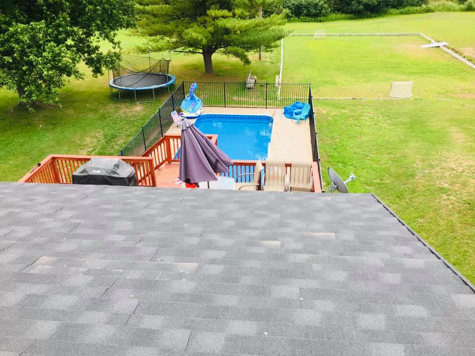 Backyard with a pool, deck, trampoline, slide, and green lawn viewed from a roof.